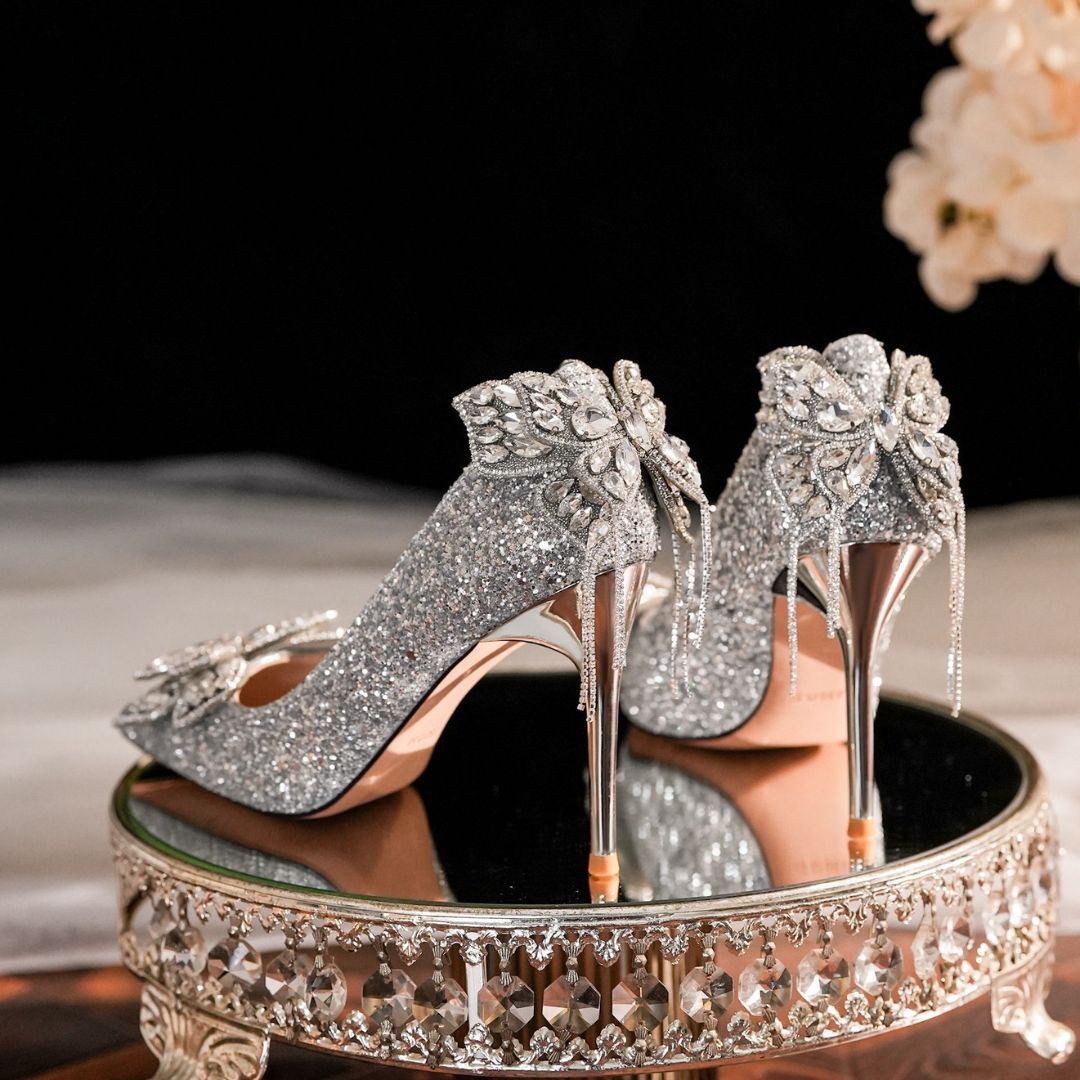 Silver glitter high-heeled shoes with floral embellishments on a decorative stand.