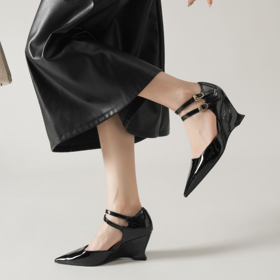 Black patent leather shoes worn with a black outfit on a light background