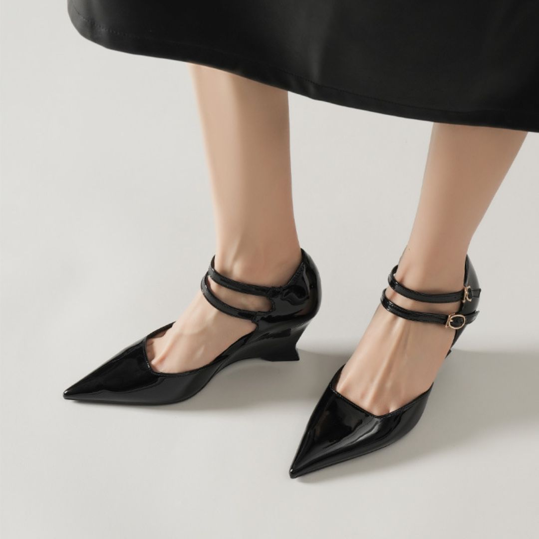 Black patent leather shoes with thin straps worn by a person in a black skirt.
