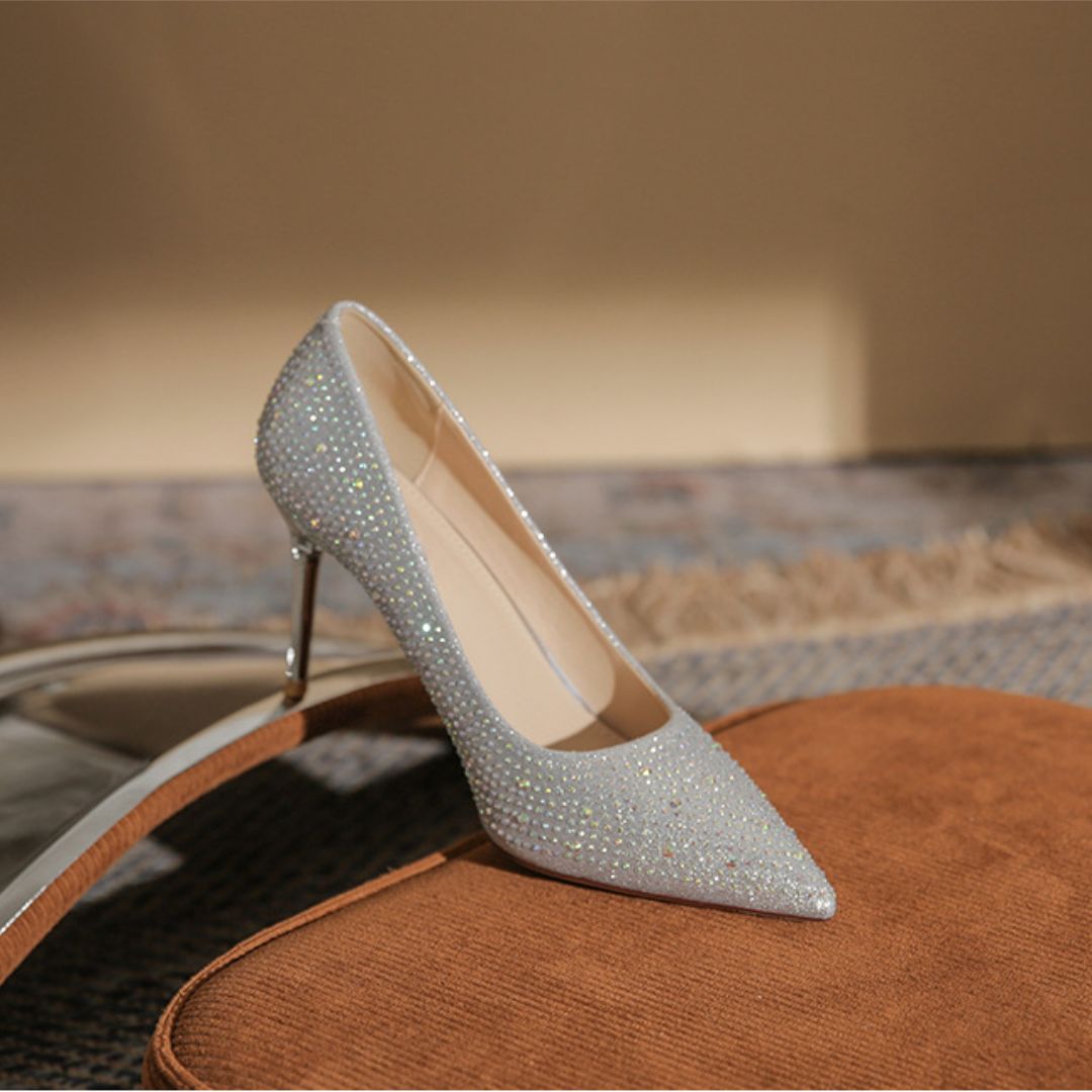 Silver stiletto shoe with rhinestone details on a textured surface