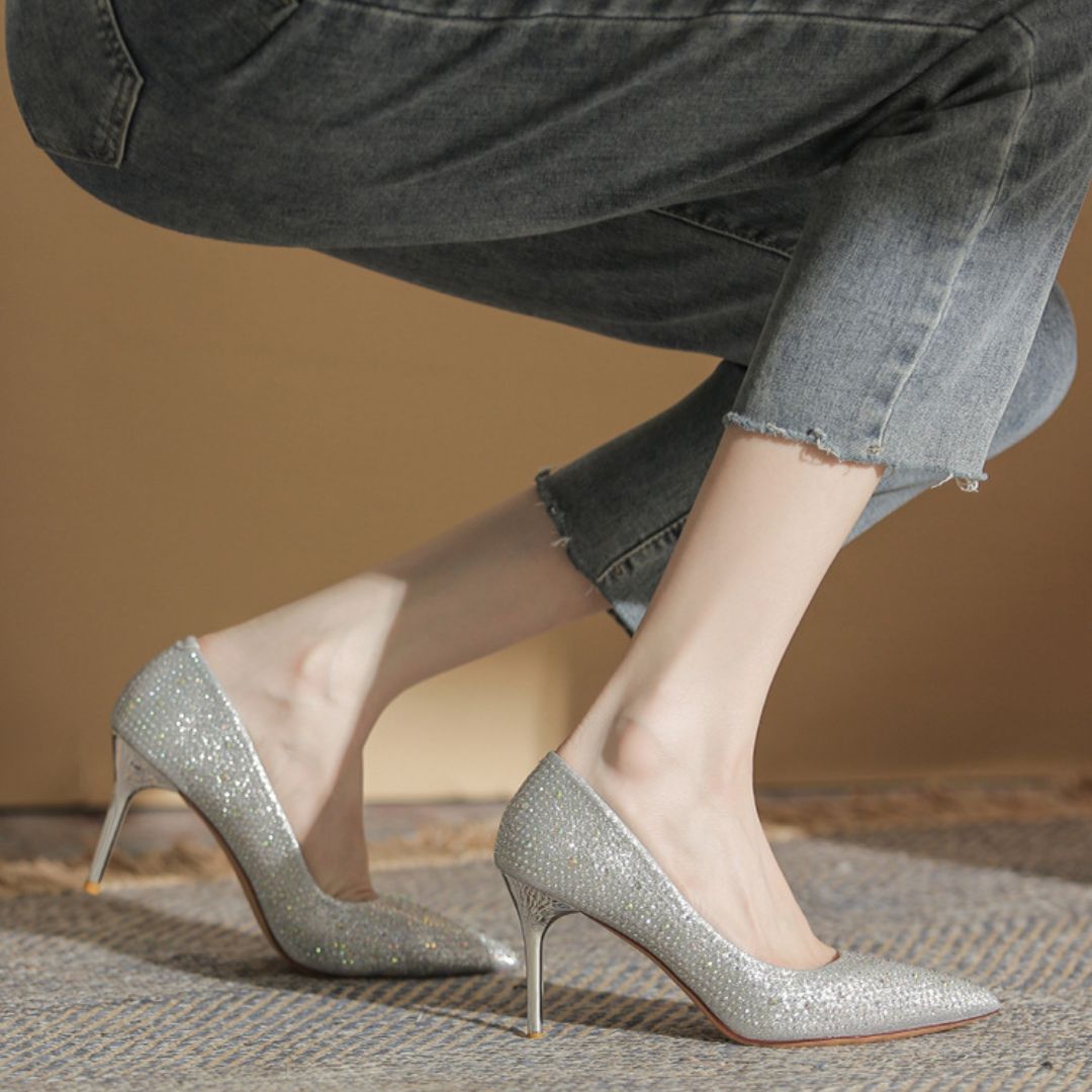 Silver glitter high heels worn with jeans on a neutral background