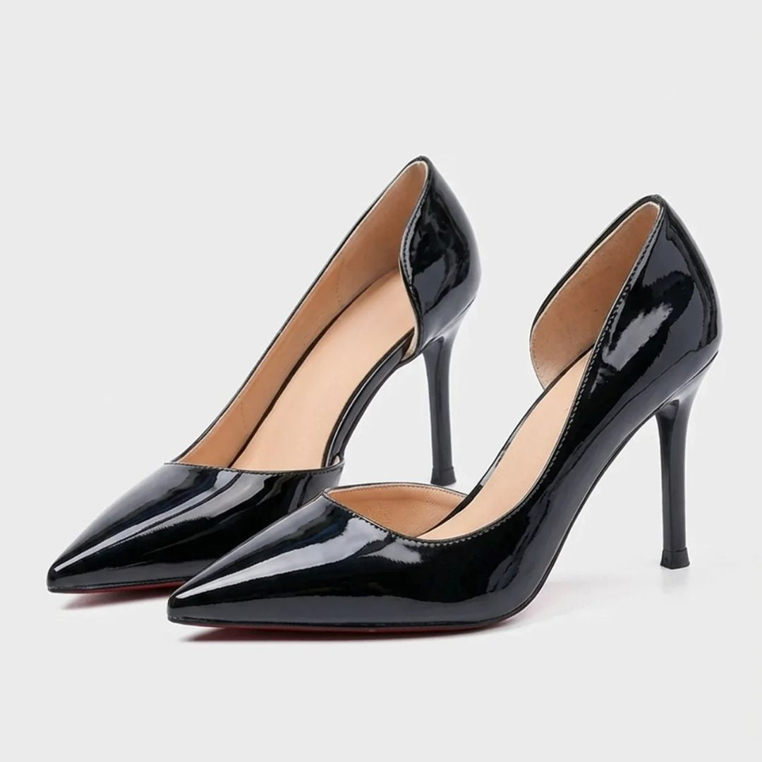 Pair of black patent leather high heels on a light gray background