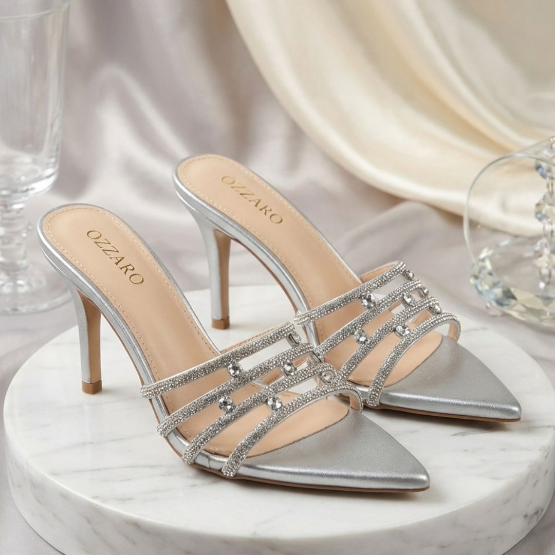 Silver high-heeled shoes with embellishments on a marble surface.